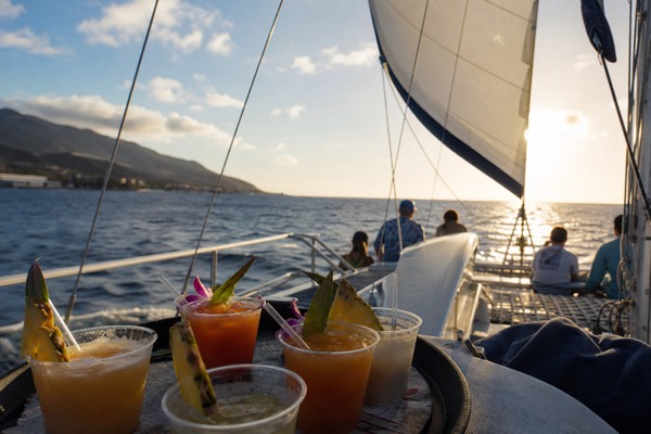Sailing catamaran heeling gently at sunset off Maui with cocktail glasses in the foreground