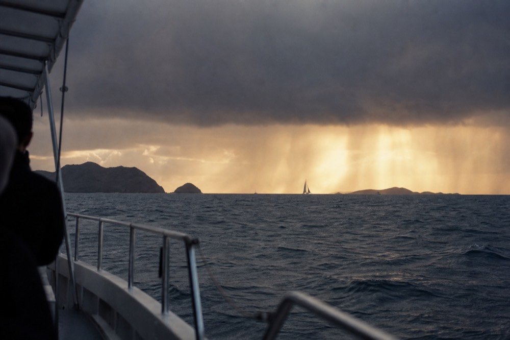 A short rain squall crossing a channel at dusk, gold light breaking under the cloud base and lighting the water beneath it