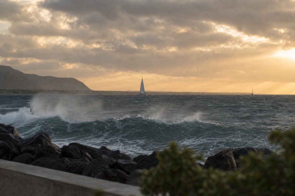Choppy whitecapped water just outside a harbour breakwater under strong afternoon wind, spray lifting off a wave crest