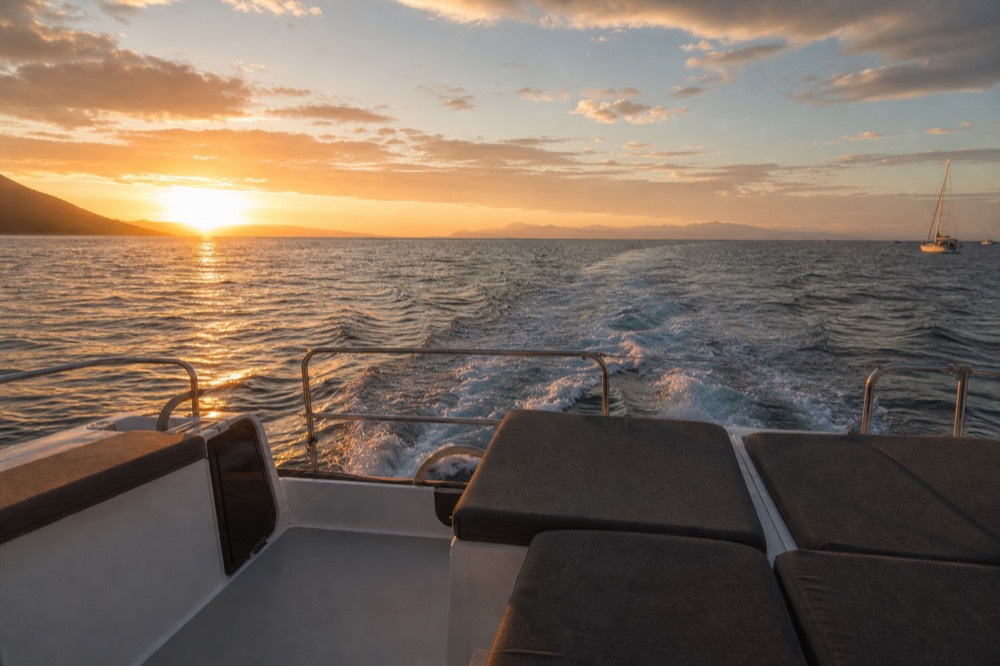 The aft bench seating of a large sailing catamaran, low to the water, empty cushions and a straight wake trailing behind