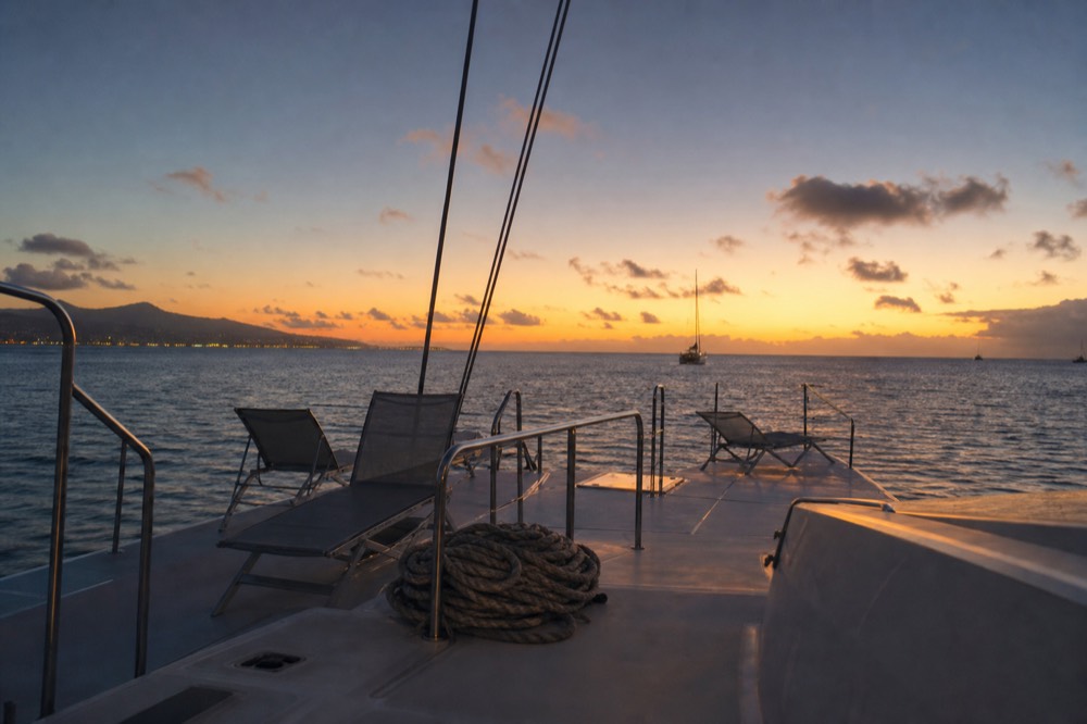 Empty deck chairs and a coiled mooring line on a boat's aft deck as the sky fades from orange to deep blue after sundown