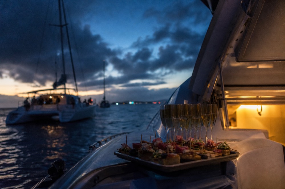 A tray of passed appetizers and a row of full glasses on a boat's bar counter, warm low light coming through an open hatch