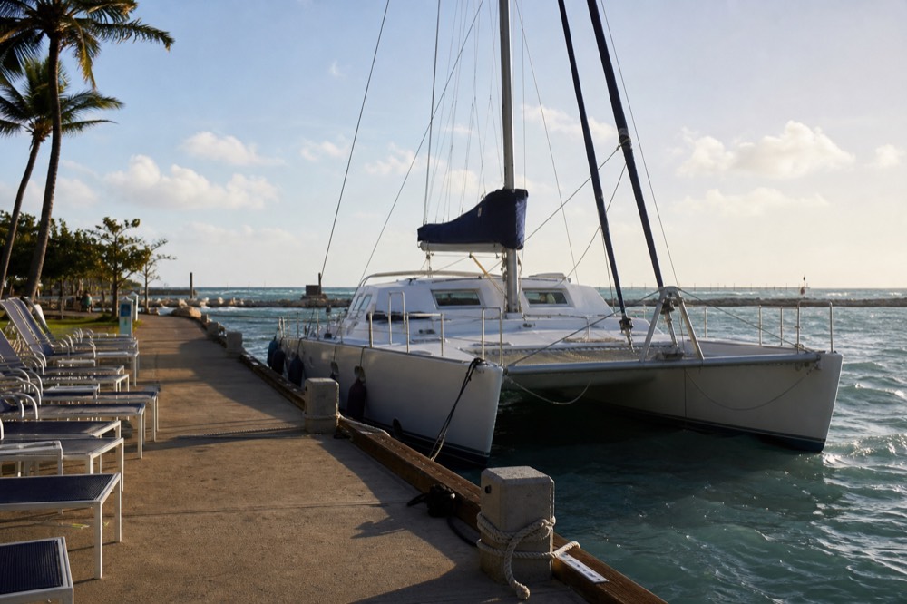 Harbor slip in late afternoon with a catamaran tied up and empty seats waiting under long shadows across the dock