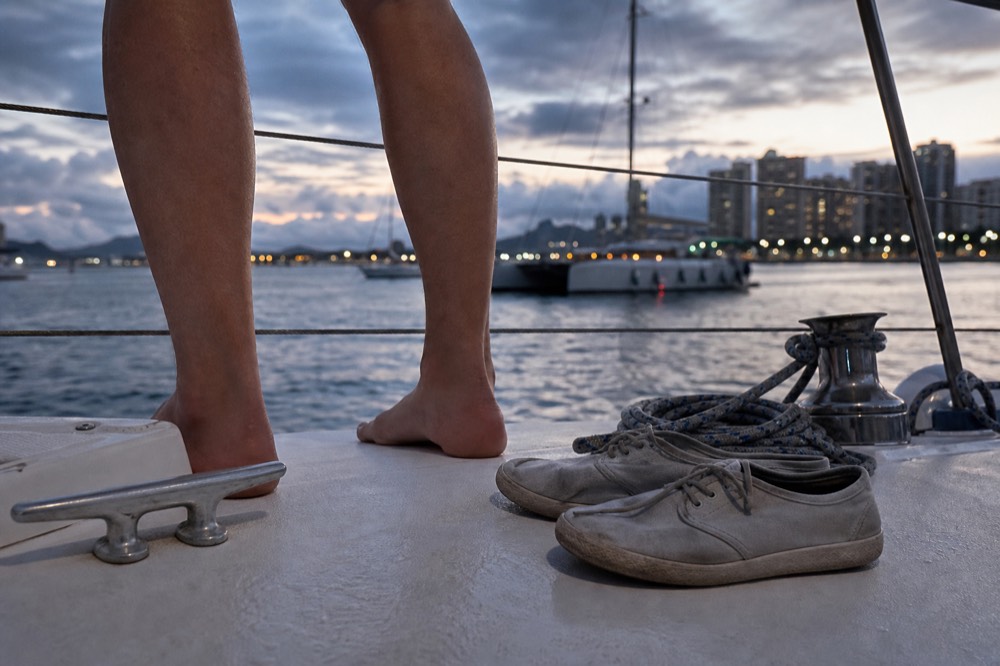 Close view of bare feet and flat deck shoes on a wet white boat deck beside a cleat and coiled line
